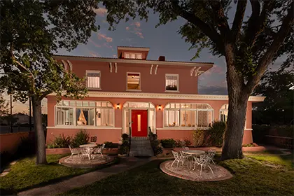 A two-story peach-colored house at twilight with a bright red front door and patio furniture on the lawn.