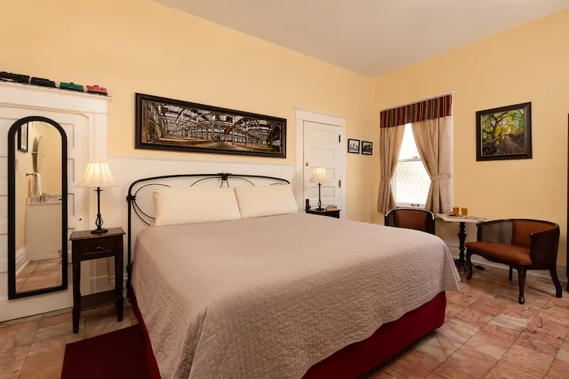 A cozy hotel room featuring a king bed with a light-colored quilt, pale yellow walls, and tile flooring.