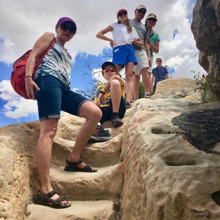 A low-angle shot of six people hiking up rock-carved stairs under a cloudy sky.