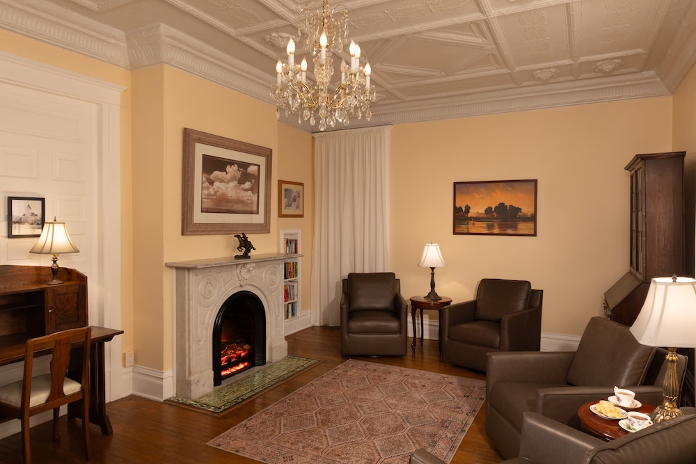 A traditional living room with cream walls, a stone fireplace, crystal chandelier, and comfortable brown armchairs.