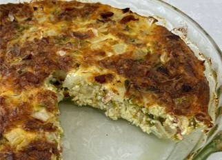A baked egg dish in a glass pie dish with a large wedge missing, showing a textured filling of cheese and vegetables.