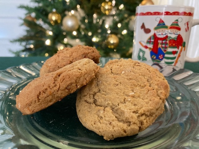 Three plain cookies on a glass plate with a festive Christmas mug and a blurred tree in the background.