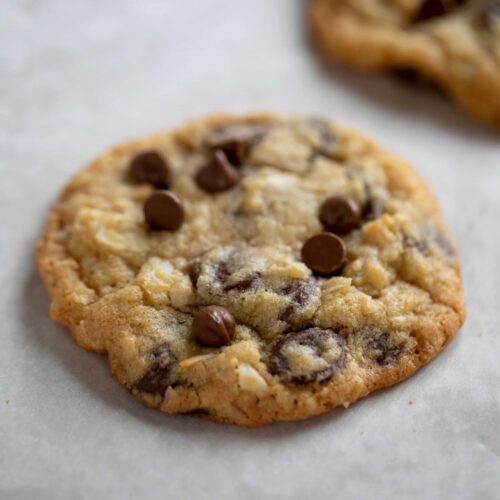 Two chocolate chip cookies resting on a sheet of white parchment paper.