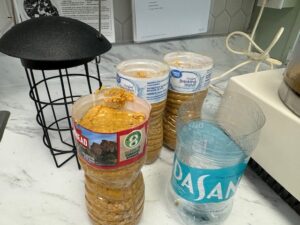 Plastic bottles filled with peanut butter, a cage bird feeder, and an empty Dasani water bottle on a white counter.