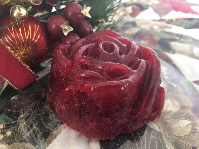 A dark red, rose-shaped molded gelatin or cranberry dish sits next to holiday decorations on a patterned surface.