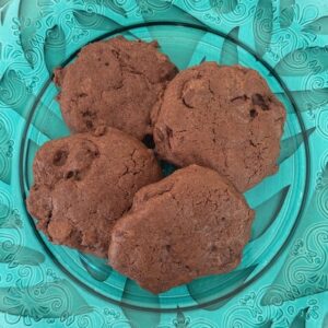 Four chocolate cookies arranged on a circular glass plate with a decorative teal floral pattern border.