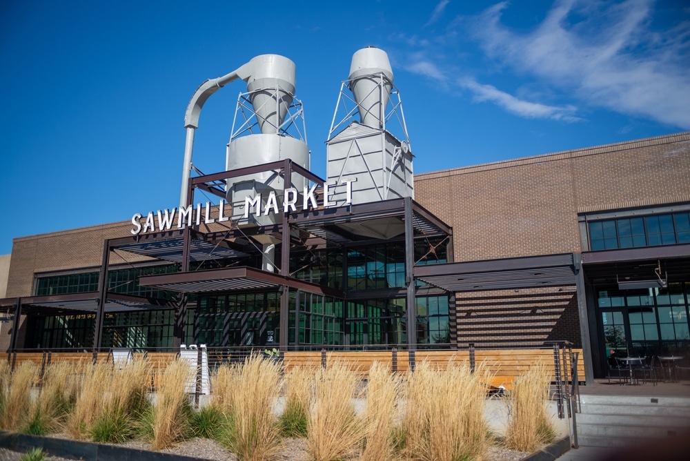 The Sawmill Market building features industrial silos and a brick exterior under a blue sky.