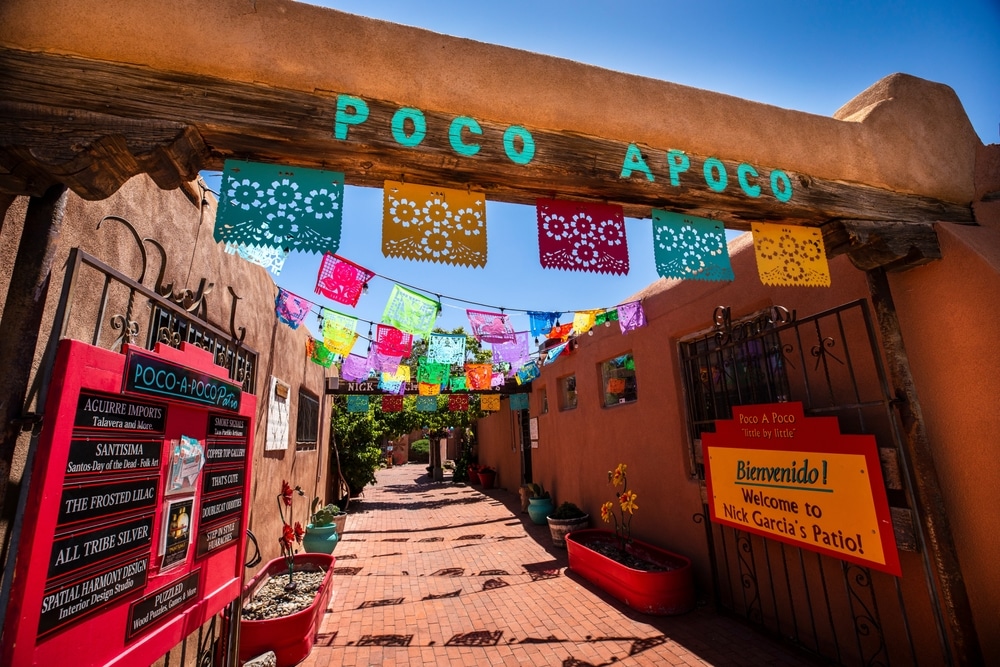 An adobe-style entrance with "POCO APOCO" in turquoise letters, decorated with colorful papel picado banners.