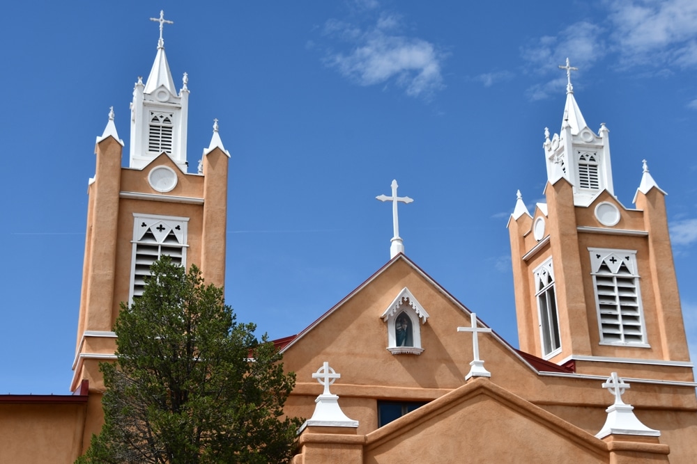 An adobe-style church with two towers and several white crosses against a clear blue sky.