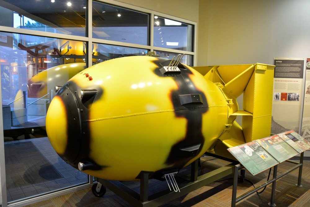 A yellow and black model of the Fat Man atomic bomb on display in a museum with informational placards nearby.