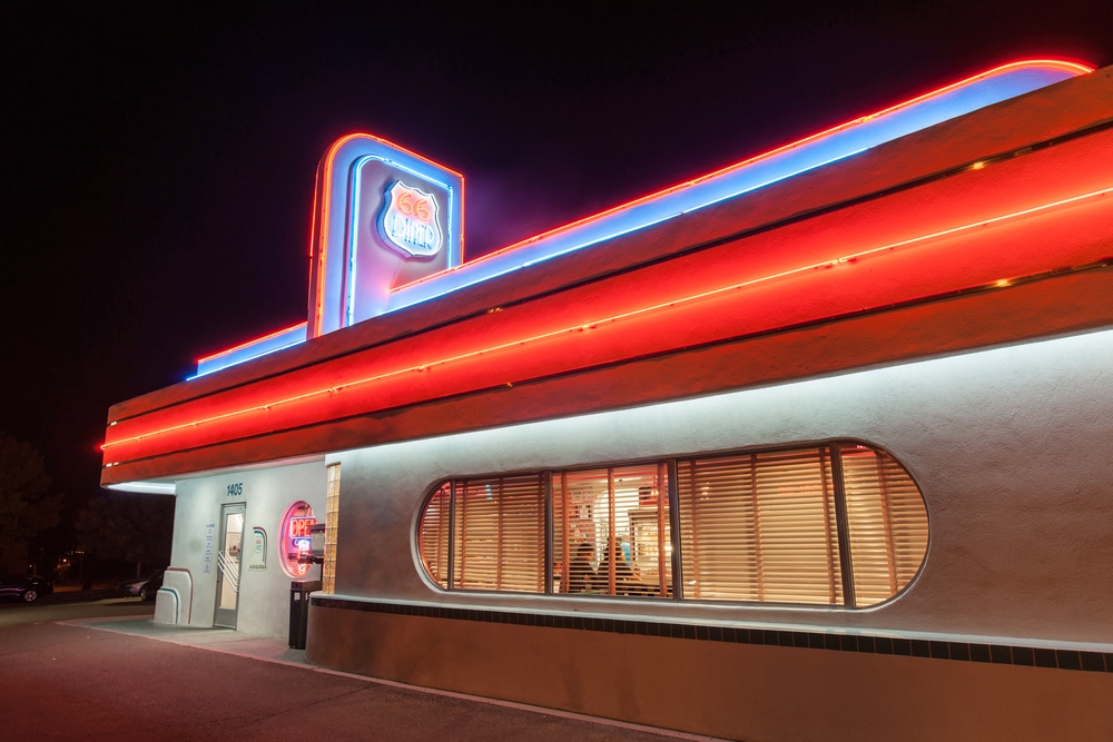A diner building at night with glowing red and blue neon lights and an oval-shaped window.