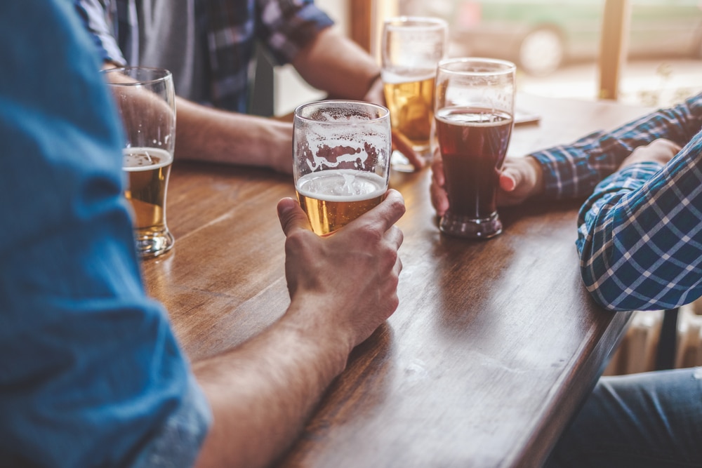 Three people sit at a wooden table, each holding a glass of beer.