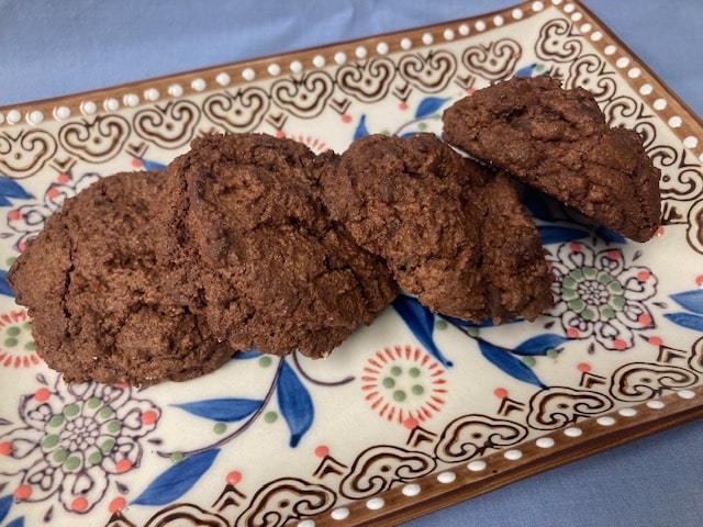 Four dark chocolate cookies rest on a rectangular, white decorative plate with blue and floral patterns.